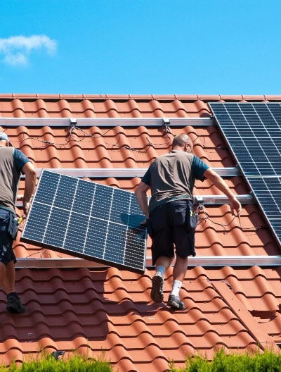 Mitarbeiter einer Solaranlagen-Firma tragen ein Solarmodul auf ein Dach