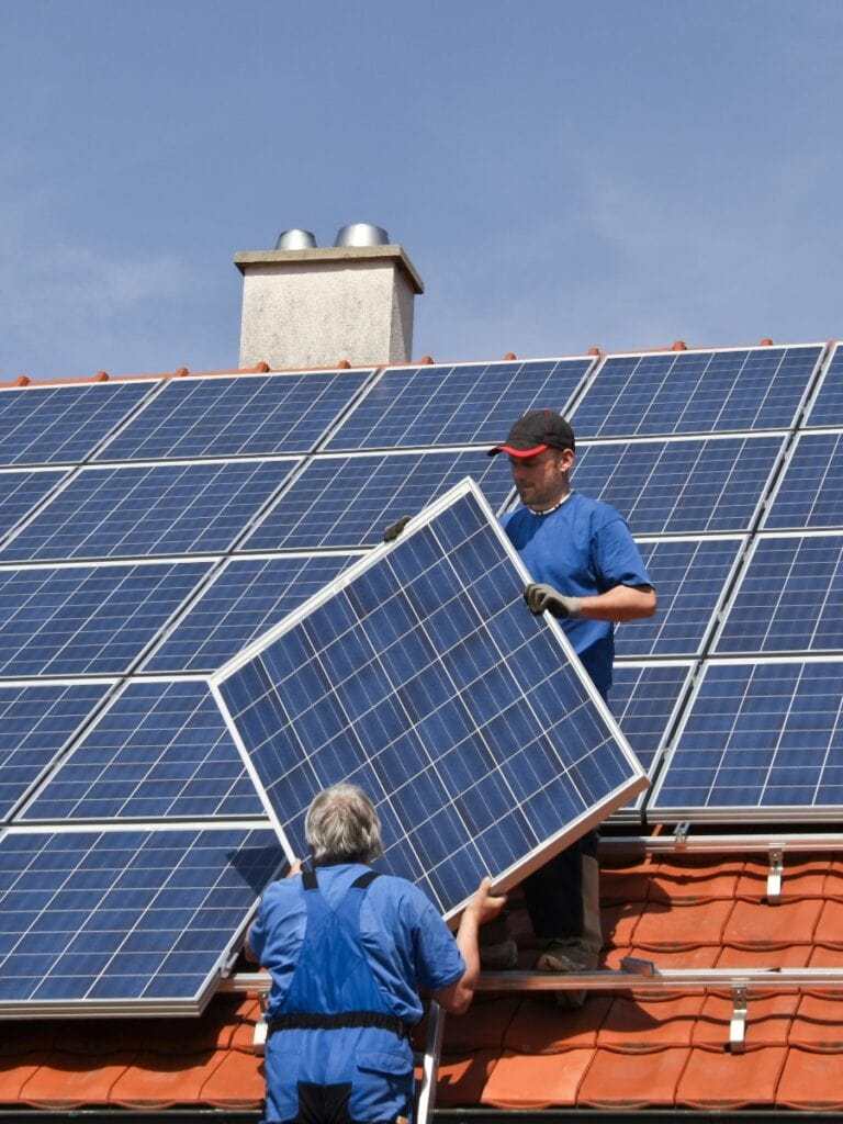 Zwei Mitarbeiter montieren Solarpanel einer Solaranlage auf rotem Ziegeldach