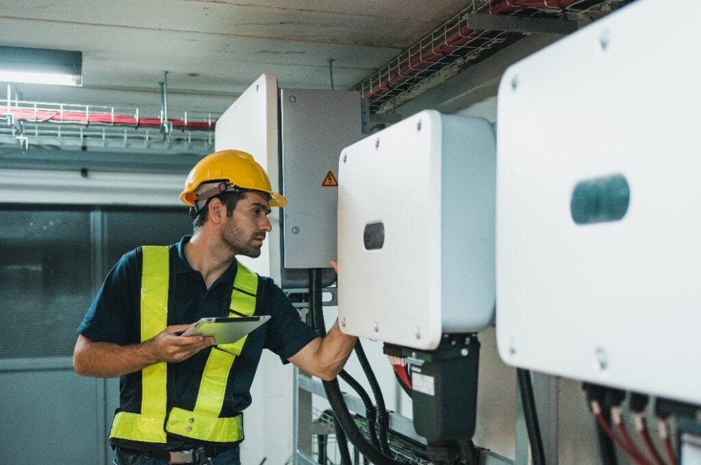 Techniker beim Einrichten eines Wechselrichter-Solarmoduls im Elektroraum. Servicetechniker bei der Installation einer Solarzelle auf dem Dach einer Fabrik. Konzept für saubere und erneuerbare Energie.